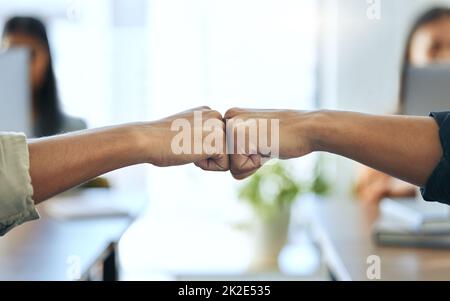 Das können wir gemeinsam tun. Eine kurze Aufnahme von zwei nicht erkennbaren Geschäftsleuten, die zusammen im Büro sitzen und sich gegenseitig eine Faustfalle geben. Stockfoto