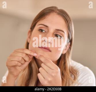 Ich bin mir sicher, dass das verschwinden wird, wenn ich es auslasse Kurzer Schuss einer jungen Frau, die einen Pickel auf ihr Gesicht quetscht. Stockfoto