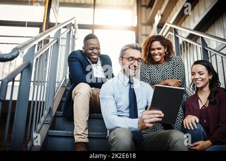 Manchmal sind spontane Meetings die besten. Aufnahmen aus dem niedrigen Winkel einer Gruppe von Kollegen, die spontan ein Meeting mit einem Tablet auf der Treppe hatten. Stockfoto