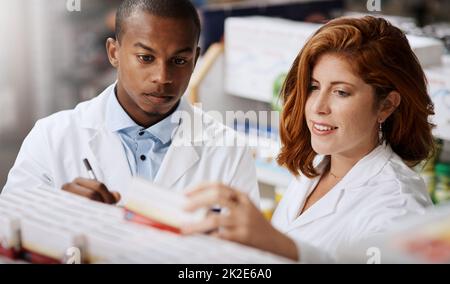 Aktualisieren aller Lagerbestände in ihren Regalen. Aufnahme von zwei Apothekern, die in einem Chemiker zusammenarbeiten. Stockfoto