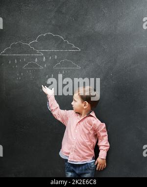 Wettermann der Zukunft. Ein kleiner Junge zeigt Zeichnungen von Regenwolken auf einer Tafel. Stockfoto