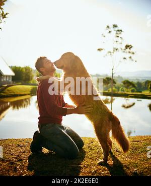 Was für ein großer Junge. Ganzkörperaufnahme eines hübschen jungen Mannes und seines Hundes, der den Tag an einem See im Park verbringt. Stockfoto