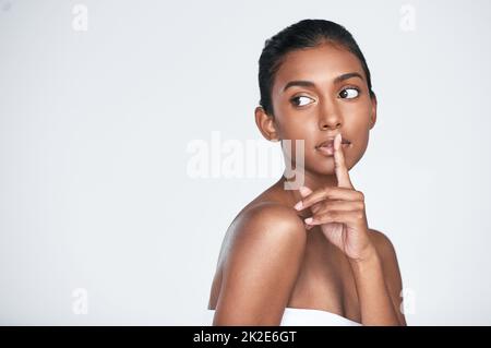 Jeder möchte wissen, was mein Geheimnis ist. Aufnahme einer schönen jungen Frau, die vor weißem Hintergrund posiert. Stockfoto