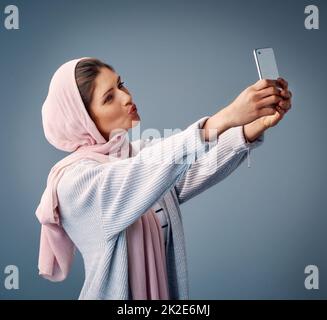 Sie nimmt die perfekten Selfies. Studioaufnahme einer attraktiven jungen Frau, die Selfies macht, während sie vor einem grauen Hintergrund steht. Stockfoto