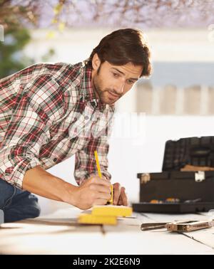 Fachkundiger Heimwerker. Ein hübscher junger Zimmermann, der etwas Holz misst. Stockfoto