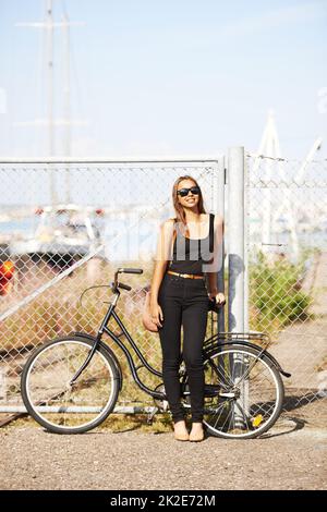 Ich werde den Fang des Tages sehen. Eine schöne junge Frau, die am Hafen vor ihrem Fahrrad steht. Stockfoto