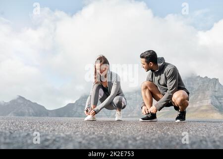 Unsere Laufschuhe haben Magie in sich. Aufnahme eines sportlichen jungen Mannes und einer jungen Frau, die beim Training im Freien ihre Schnürsenkel binden. Stockfoto