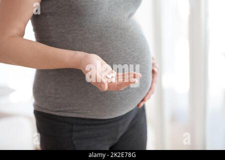 Pränatale Vitamine sind wichtig für die richtige Entwicklung. Kurzer Schuss einer Schwangeren, die Tabletten in der Hand hält, während sie zu Hause steht. Stockfoto