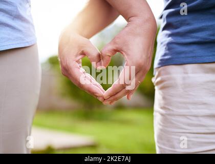 Gemeinsam bilden wir ein starkes Herz. Nahaufnahme von zwei unbekannten Menschen, die ein Herz bilden, zusammen mit ihren Händen, während sie tagsüber in einem Park draußen stehen. Stockfoto