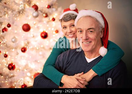 Wir wünschen Ihnen einen Frohe Weihnachten. Ein zugeschnittenes Porträt eines glücklichen reifen Paares vor einem Weihnachtsbaum. Stockfoto