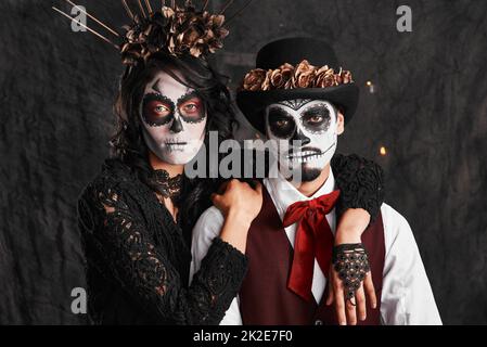 Wir hörten, wie wir unsere Vorfahren feierten. Verkürztes Porträt eines liebevollen jungen Paares in ihren mexikanischen Halloween-Kostümen. Stockfoto