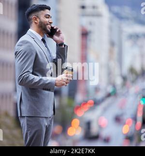 Überlassen Sie mir die Verhandlungen. Aufnahme eines hübschen jungen Geschäftsmannes, der allein stand und sein Handy benutzte, während er eine Tasse Kaffee genoss. Stockfoto