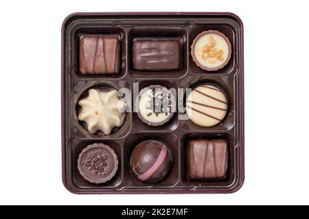 Nahaufnahme einer Schachtel mit feinen Schokoladenbonbons in einer wunderschönen Plastikbox isoliert auf weißem Hintergrund. Überraschungsgeschenk zum Valentinstag oder zu anderen festlichen Anlässen. Makro. Stockfoto