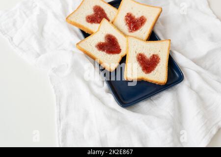 Toast, auf dem das Herz aus Marmelade besteht. Überraschendes Frühstückskonzept im Bett. Romantik für St. Valentinstag, ein Ort für eine Inschrift. Stockfoto