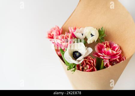 Wunderschönes rot-weißes Strauß aus Tulpen und Anemonen in Kraftpapier. Frühlings- und Blütebegriff. Mit Kopierbereich. Stockfoto