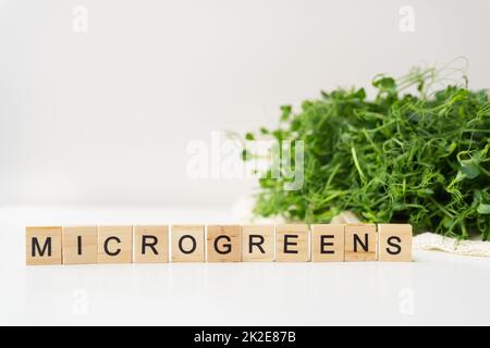 Gemüseerbsensprossen, Mikrogrün auf weißem Hintergrund, vegane Gesundheit Superfood. Aufschrift aus Holzbuchstaben mikrogrün. Stockfoto