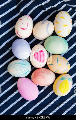 Wunderschöne Ostereier, die mit Aquarellen bemalt sind, liegen auf einem gestreiften blauen Stoff. Osterferienkonzept. Stockfoto