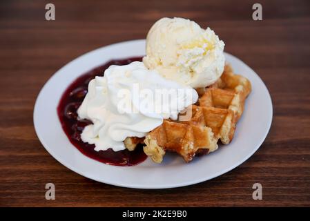 Eine heiße Waffel mit Kirschen, Eis und Schlagsahne. Stockfoto