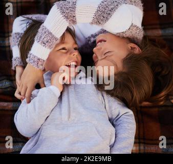 Du bist mein Bruder und mein bester Freund. Hochknieige Aufnahme eines niedlichen kleinen Mädchens, das ihren Bruder umarmt, während sie auf einer Decke zusammen liegen. Stockfoto