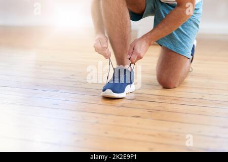 Gute Schuhe bringen dich an die richtige Stelle. Kurzer Schuss eines Mannes, der seine Schnürsenkel in einem Fitnessstudio bindet. Stockfoto