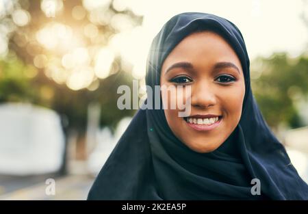 An unseren Wurzeln festhalten. Porträt einer fröhlichen jungen Frau, die tagsüber allein steht und vor der Kamera lächelt. Stockfoto