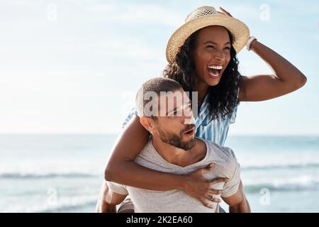 Sehen Sie sich die Sehenswürdigkeiten rund um das Meer an. Aufnahme eines jungen Mannes mit Huckepack seiner Freundin am Strand. Stockfoto