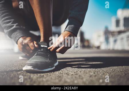 Das beste Projekt, an dem Sie je arbeiten werden, sind Sie. Aufnahme eines sportlichen Mannes, der seine Schnürsenkel vor einem Lauf bindet. Stockfoto