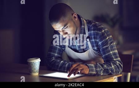 Er hat den Antrieb, jederzeit Aufgaben zu erledigen. Aufnahme eines jungen Mannes, der spät in seinem Café an einem digitalen Tablet arbeitete. Stockfoto