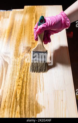 Die Massivplatte wird mit einem Pinsel mit Holzflecken versehen Stockfoto