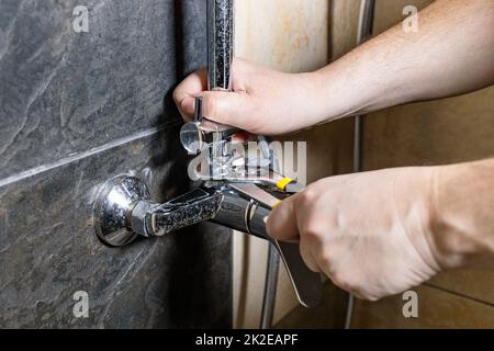 Der Klempner repariert alten Duschhahn an der gefliesten Wand Stockfoto