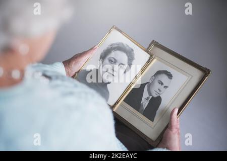 Blick durch Schnappschüsse aus der Vergangenheit. Ausgeschnittene Aufnahme einer älteren Frau, die alte Schwarz-Weiß-Fotos von einem Mann und einer Frau ansieht. Stockfoto