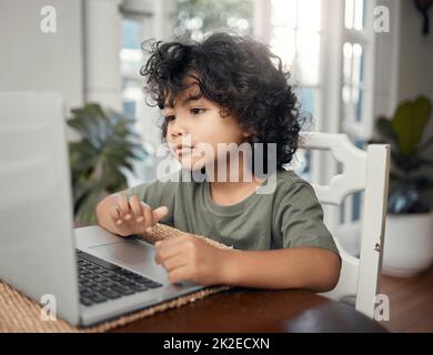 Lernen mit meinem Lieblingscharakter. Aufnahme eines entzückenden kleinen Jungen, der einen Laptop benutzt, während er zu Hause sitzt. Stockfoto