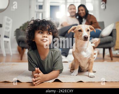 Chillen mit meinem Lieblingsbegleiter. Aufnahme eines kleinen Jungen, der sich mit seinem Hund verklebt, während seine Eltern im Hintergrund sitzen. Stockfoto