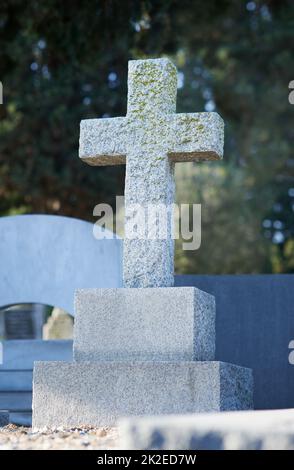 Das Kruzifix ist der Hüter dieses Grabes. Aufnahme eines Grabsteins auf einem Friedhof. Stockfoto