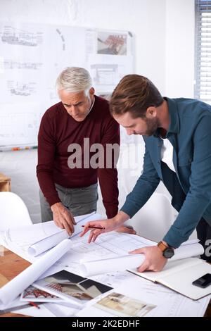 Die letzten Feinheiten auf die Pläne zu setzen. Eine kurze Aufnahme von zwei männlichen Architekten, die in ihrem Büro zusammenarbeiten. Stockfoto