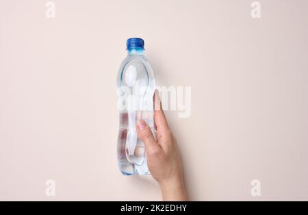 Weibliche Hand hält eine transparente Plastikflasche auf einem beigen Hintergrund Stockfoto