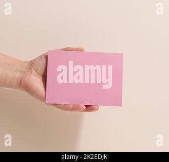 Weibliche Hand mit leerem rosa Papier auf beigem Hintergrund. Kopieren Bild oder Text einfügen, Nahaufnahme Stockfoto