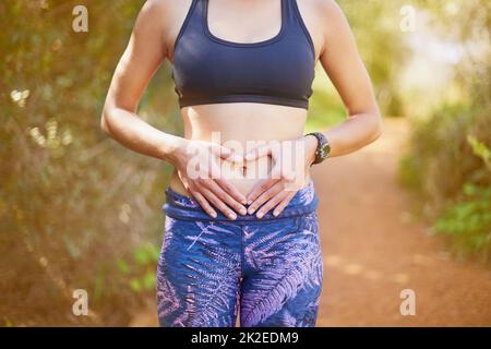 Liebe deinen Körper und er wird dich wieder lieben. Aufnahme einer sportlichen jungen Frau, die eine Herzform auf bildet. Stockfoto