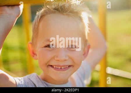 Fröhliche Kindheitstage. Porträt eines lächelnden kleinen Jungen, der in einer Dschungelturnhalle im Park spielt. Stockfoto
