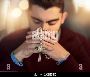 Ich kann es nicht alleine machen. Aufnahme eines jungen Mannes, der alleine betet, während er einen Rosenkranz hält. Stockfoto