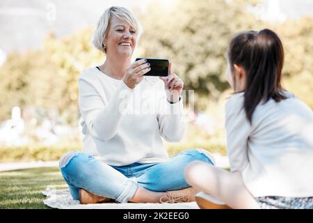 Oma möchte so viele Erinnerungen mit ihr festhalten. Aufnahme einer Großmutter, die im Freien Fotos von ihrer Enkelin machte. Stockfoto