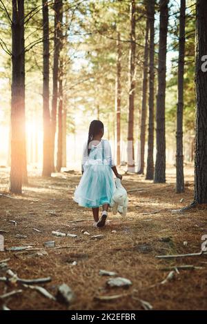 Auf einer Erkundung der Wunder der Wälder. Rückansicht eines kleinen Mädchens, das mit ihrem Teddybären im Wald spazierengeht. Stockfoto