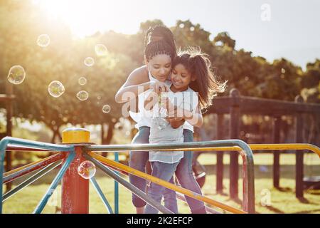 Lasst uns versuchen, einen großen zu blasen. Ein kurzer Schuss einer Mutter und ihrer Tochter, die Blasen in den Park blasen. Stockfoto