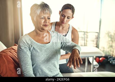 Die physiotherapeutische Rehabilitation zielt darauf ab, die Funktion und das Wohlbefinden der Patienten zu optimieren. Aufnahme einer älteren Frau, die von einem Physiotherapeuten behandelt wird. Stockfoto
