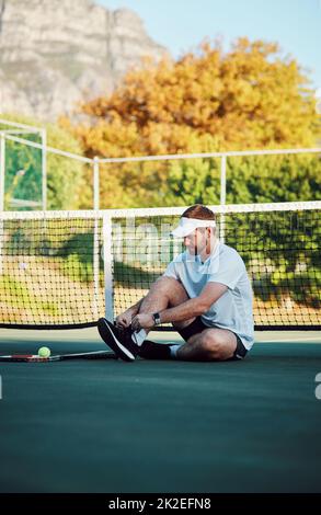 Profis bereiten sich immer gut vor. Aufnahme eines sportlichen jungen Mannes, der seine Schnürsenkel auf einem Tennisplatz bindet. Stockfoto