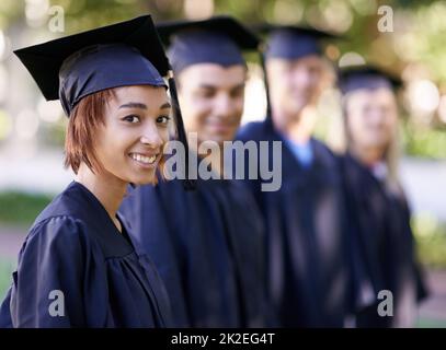 Gespannt auf das, was kommen wird. Eine Gruppe lächelnder Absolventen steht in einer Reihe und schaut auf die Kamera. Stockfoto