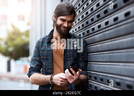 Verbindet euch durch jeden Lebensabschnitt. Aufnahme eines hübschen jungen Mannes, der sein Handy benutzte, während er durch die Stadt ging. Stockfoto