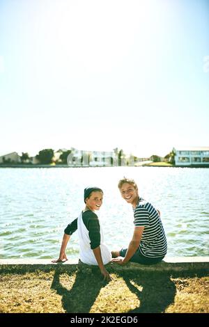 Es ist ein tolles Leben in der Nähe der Lagune. Porträt von zwei jungen Brüdern, die draußen an einer Lagune sitzen. Stockfoto