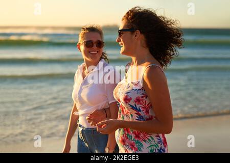 Wer einen Strandtag mit Bestie nicht mag. Eine kurze Aufnahme von zwei attraktiven jungen Freundinnen, die sich beim Strandspaziergang unterhalten. Stockfoto