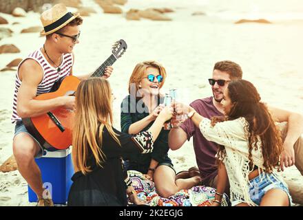 Sie lieben seine Musik. Aufnahme eines jungen Mannes, der für seine Freunde Gitarre spielt, während er am Strand chillte. Stockfoto